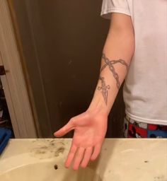 a man with a cross tattoo on his arm pointing at the sink in front of him