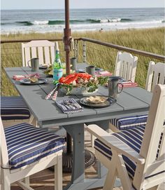 an outdoor dining table with blue and white striped chairs on the deck overlooking the ocean