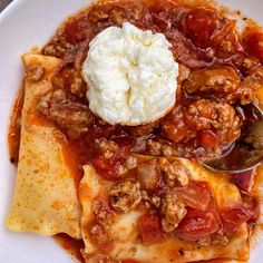 a white plate topped with tortilla shells covered in sauce and toppings next to a spoon