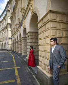 a man in a suit standing next to a woman wearing a red dress on the street