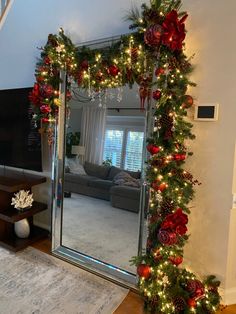 a living room decorated for christmas with lights and garland on the wall, mirror in front of it