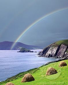 two rainbows in the sky over an ocean with hay bales on the grass