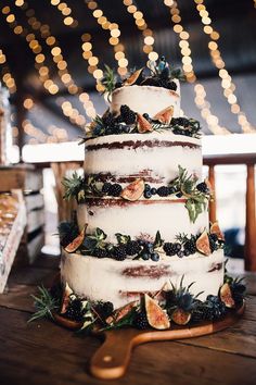 a three tiered cake with fruit and greenery on the top is sitting on a wooden table