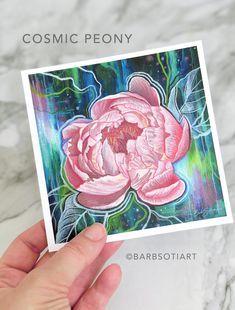 a hand holding up a card with a painting of a pink flower on it and the words cosmic peony above it