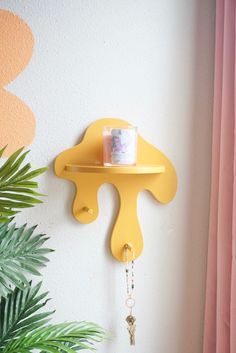 a yellow shelf with a cup on it next to a potted plant and pink curtains