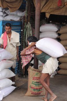 a man is carrying large bags on his back in front of a pile of sandbags