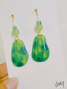 a pair of green and yellow earrings on top of a piece of paper with a hand holding