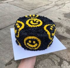 a cake with yellow and black icing on it being held by someone's hand