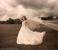 a woman in a wedding dress is posing for a photo with her veil blowing in the wind