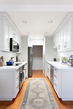 a kitchen with white cabinets and wooden floors is seen from the hallway to the dining room