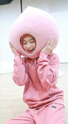 a person sitting on the floor with a large pink pillow over their head and hands