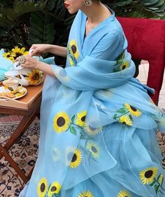 a woman in a blue dress sitting at a table with sunflowers on it