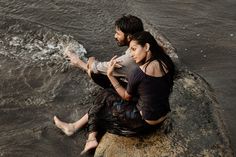 a man and woman sitting on top of a rock in the water