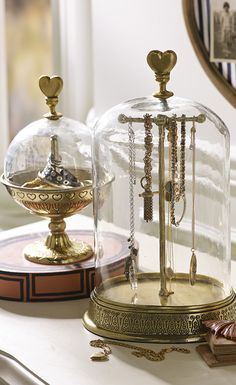 two glass domes with necklaces in them on top of a table next to a mirror