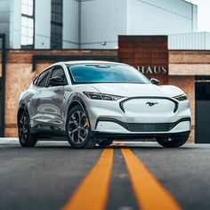 a white electric car parked on the side of a road in front of a building