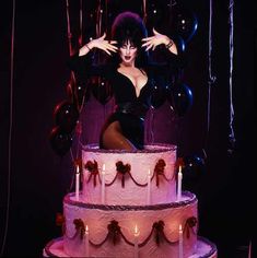 a woman sitting on top of a pink cake with balloons around her and candles in the air