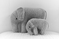 two knitted elephants standing next to each other on top of a white bed sheet