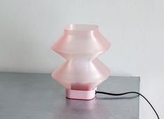 a pink lamp sitting on top of a table next to a white wall with a black cord