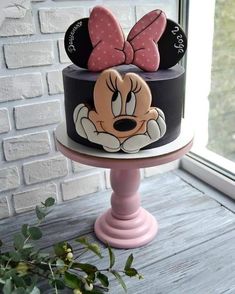 a minnie mouse cake with pink bows on top is sitting in front of a window