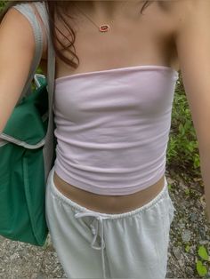 a woman in white shorts and a pink top is holding a green bag while standing outside