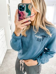 a woman taking a selfie with her phone in front of the mirror wearing a blue sweatshirt and grey sweatpants