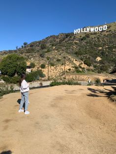 a woman standing on top of a dirt road next to a hill and hollywood sign