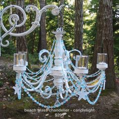 a white chandelier with blue glass beads hanging from it's sides in the woods