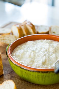 a green bowl filled with white cheese next to slices of bread