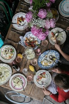 several people sitting at a table with plates of food and flowers in the background,