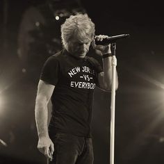 a man standing on top of a stage holding a microphone to his ear and wearing a t - shirt that says new jersey everybody