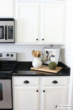 a white kitchen with black counter tops and stainless steel oven, microwave, dishwasher and toaster