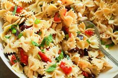 a white bowl filled with pasta salad and a serving spoon in the bowl next to it