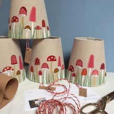 three lampshades with red and green designs on them next to some twine