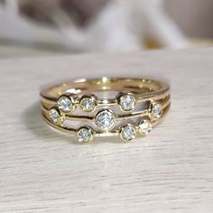 three gold wedding bands with diamonds on them sitting on a wooden table next to a white flower