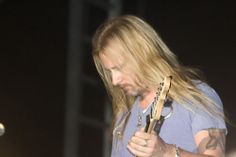 a man with long hair holding a guitar in his hand and looking down at the ground