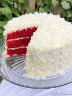 a red velvet cake with white frosting on a glass plate in front of green plants