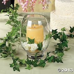 a candle is sitting in a glass vase with flowers and greenery on the table