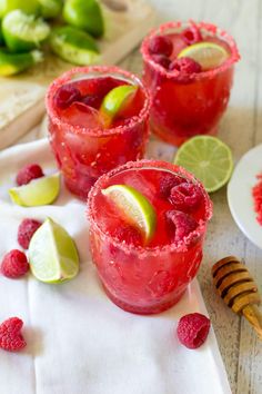 two glasses filled with raspberry margaritas on top of a white napkin next to lime slices