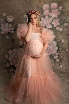 a pregnant woman wearing a pink dress and holding her hand up to her face while standing in front of flowers