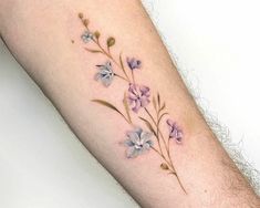 a small flower tattoo on the left forearm and arm, with purple flowers growing out of it