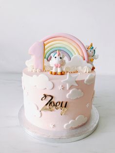 there is a pink cake decorated with unicorns and rainbows