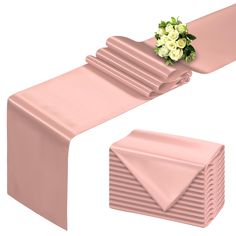 a pink table runner with white flowers on top and folded napkins in the shape of rectangles