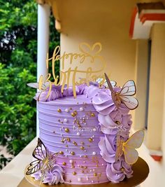 a purple cake with butterflies on it and the words happy birthday written in gold lettering