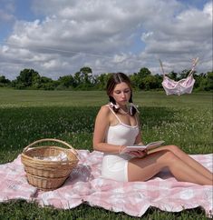 a woman sitting on top of a pink and white blanket next to a wicker basket