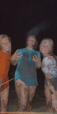 three women covered in mud standing next to each other with their arms around one another