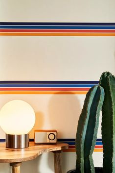 a cactus sitting on top of a wooden table next to a wall with stripes painted on it