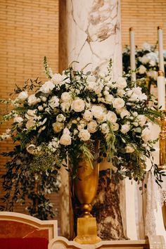 a large vase with white flowers on a table in front of a wall and candles