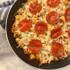 a skillet filled with pasta and pepperoni on top of a white marble counter