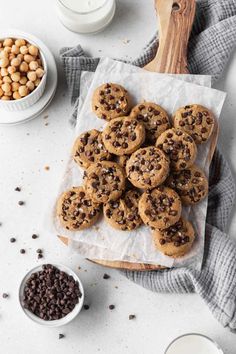 chocolate chip cookies and milk on a white table with bowls of cereal, spoons and napkin