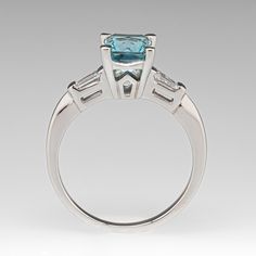 an engagement ring with a blue topazte surrounded by three baguettes in white gold